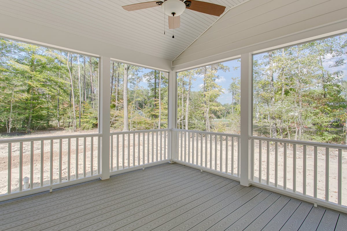 A cozy screened porch featuring a ceiling fan overlooking a serene natural landscape