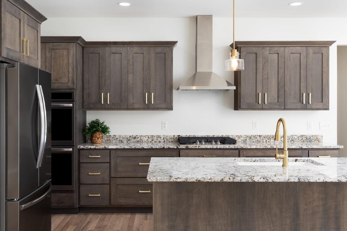 A kitchen detail with a gold faucet on a granite countertop, dark wood cabinets, stainless steel appliances
