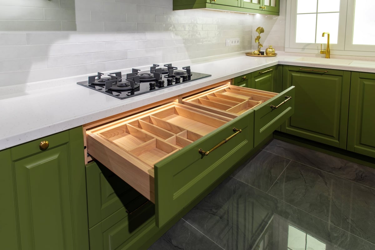 Open green kitchen cabinetry with wooden cutlery organizer interior