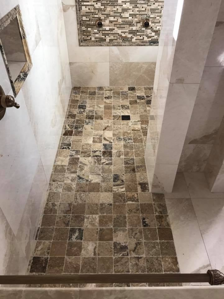 Modern bathroom shower interior with mixed brown and tan tile flooring and walls, featuring white tile accents and a decorative tile border for Pensacola bathroom remodeling