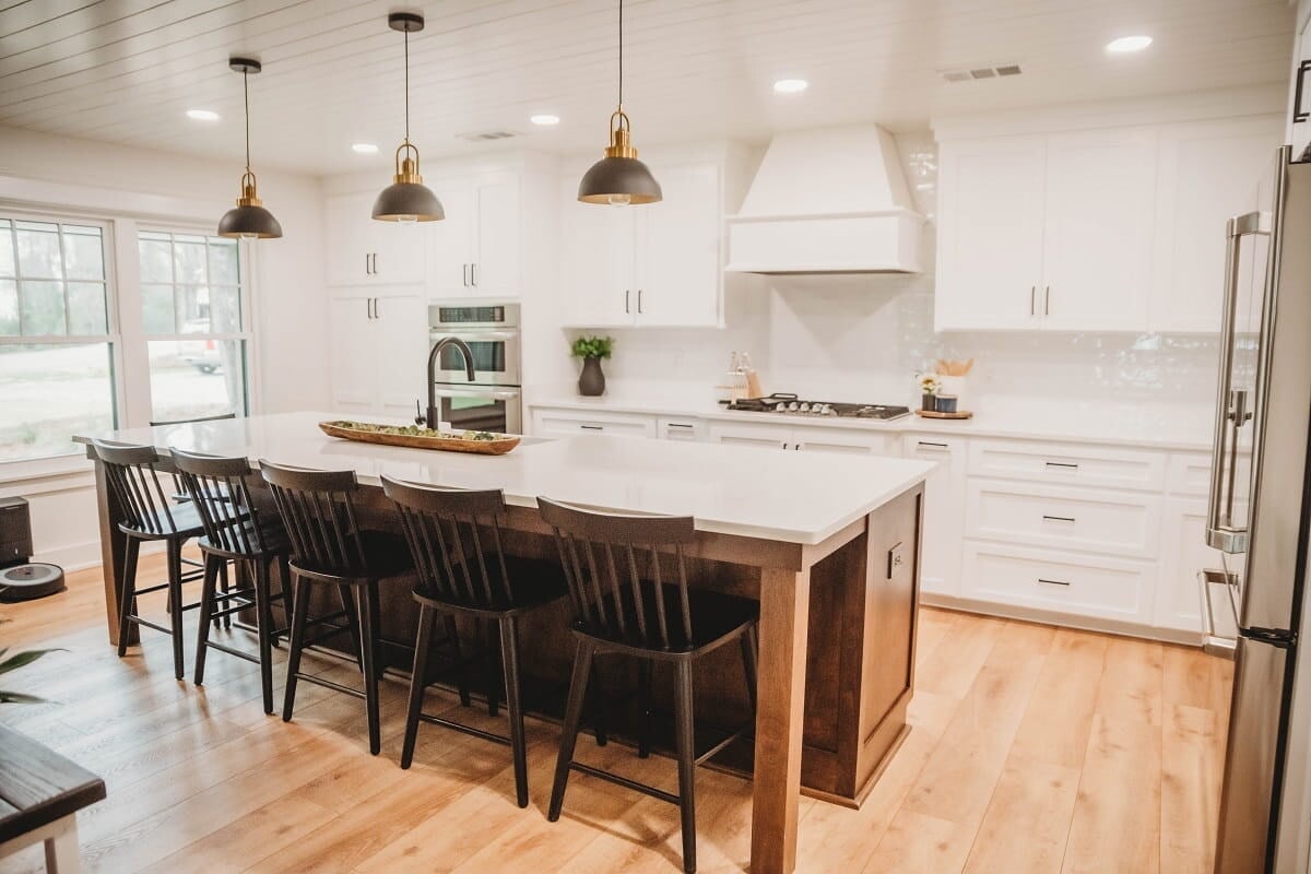 Modern white kitchen with wood island, black bar stools, brass pendant lights, white cabinets, and stainless steel appliances