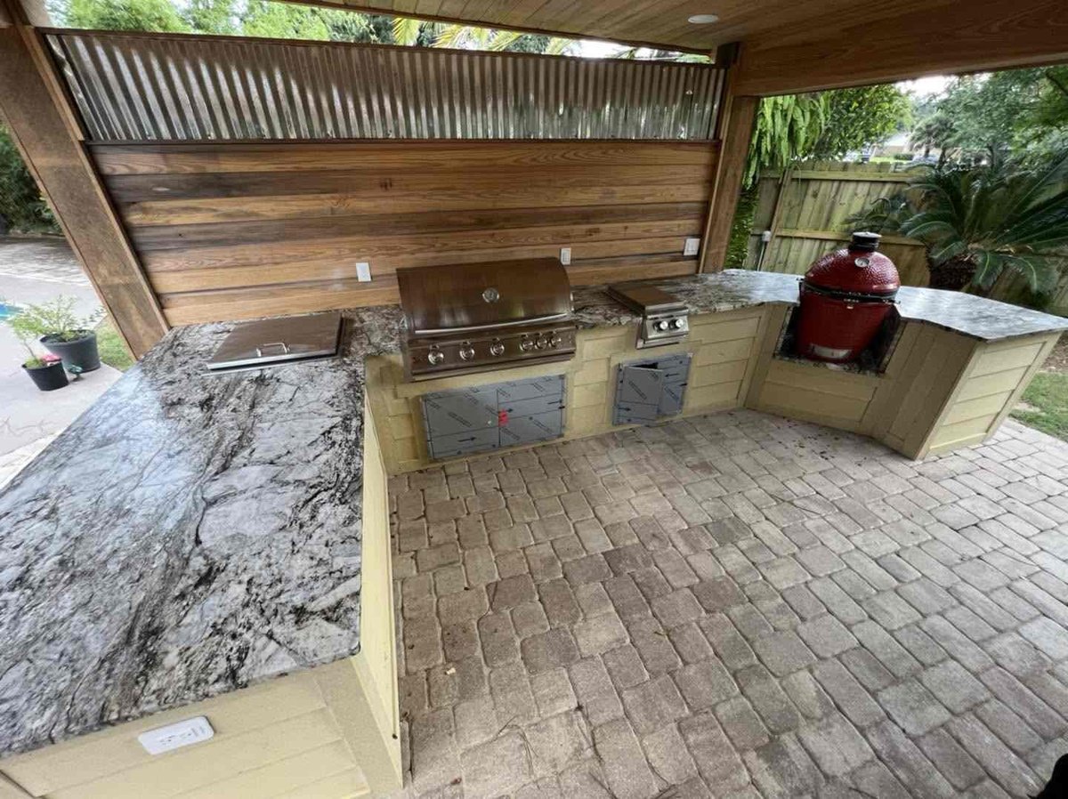 Covered outdoor kitchen with built-in grill, stovetop, and granite countertop on a brick patio