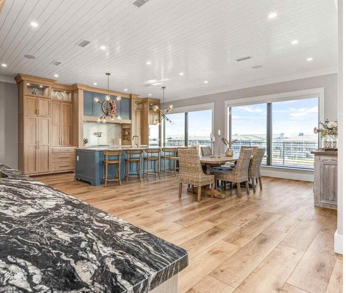Modern kitchen and dining area with marble island, wood cabinetry, bar seating, and floor-to-ceiling windows overlooking a cityscape