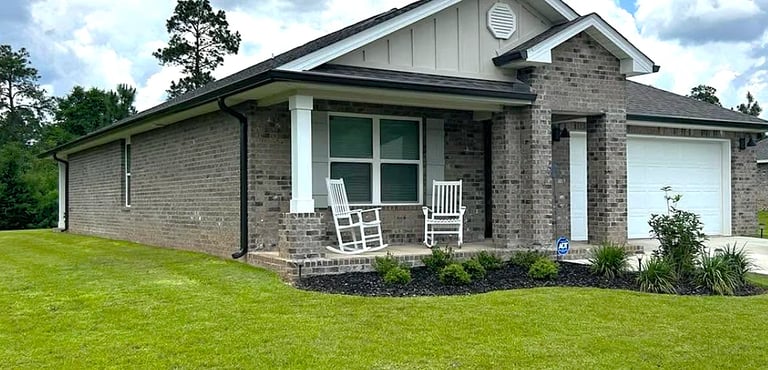 Modern single-story brick home with covered porch, white rocking chairs, and manicured green lawn