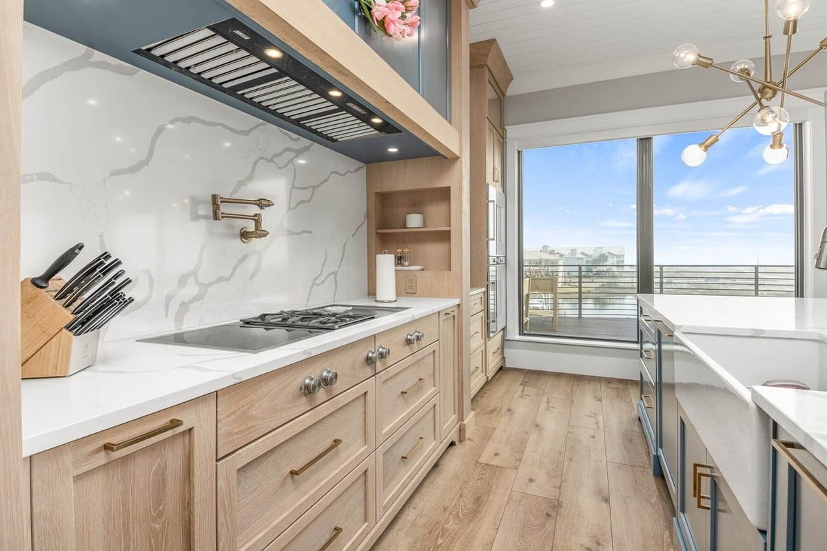 Modern kitchen with light wood cabinetry, marble countertops, gas range, and large windows overlooking a city skyline