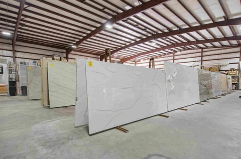Large marble slabs displayed in an industrial warehouse with metal roof and concrete floors