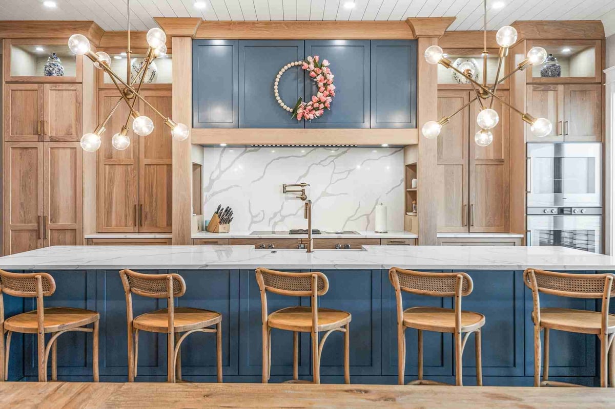 Modern kitchen with blue cabinetry, marble backsplash, wooden bar stools, and decorative wreath above range hood