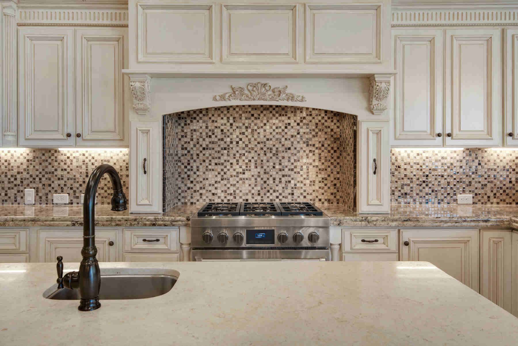 Luxury kitchen with cream cabinets, white marble countertop, stainless steel range, and decorative mosaic tile backsplash