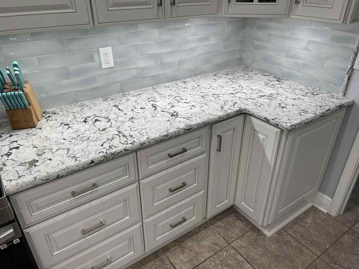Modern kitchen countertop with white speckled granite, light gray cabinetry, subway tile backsplash, and stainless steel hardware