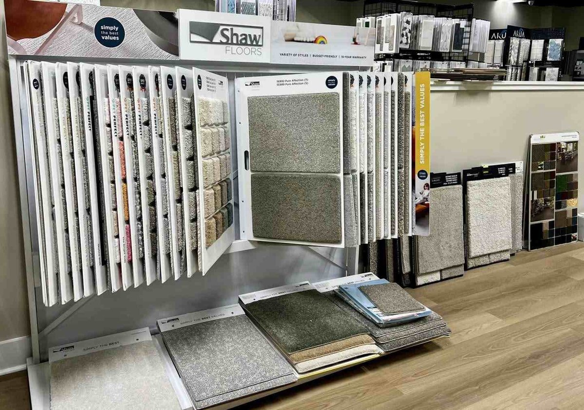 Flooring showroom display with Shaw carpet samples on large rotating stand and tile samples on wooden floor