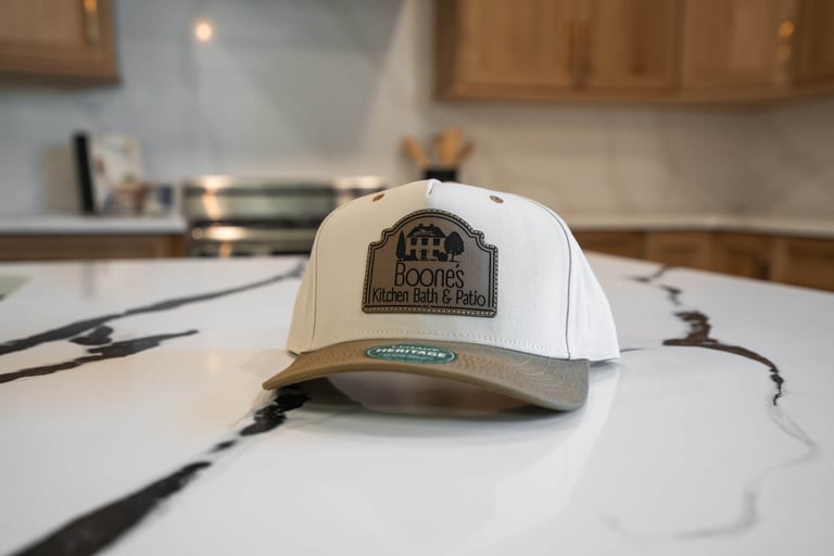 Cream and tan baseball cap with BOONES logo resting on white blueprints in a home office with wood cabinets in background