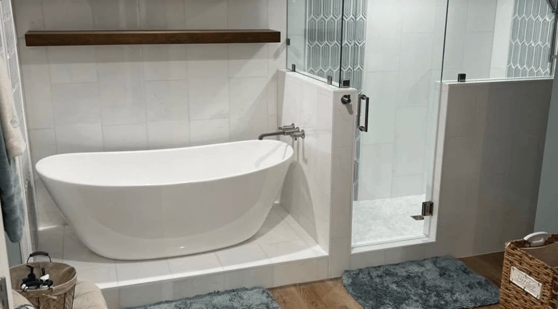 Modern bathroom interior with white freestanding oval bathtub, glass shower enclosure, and wood accents