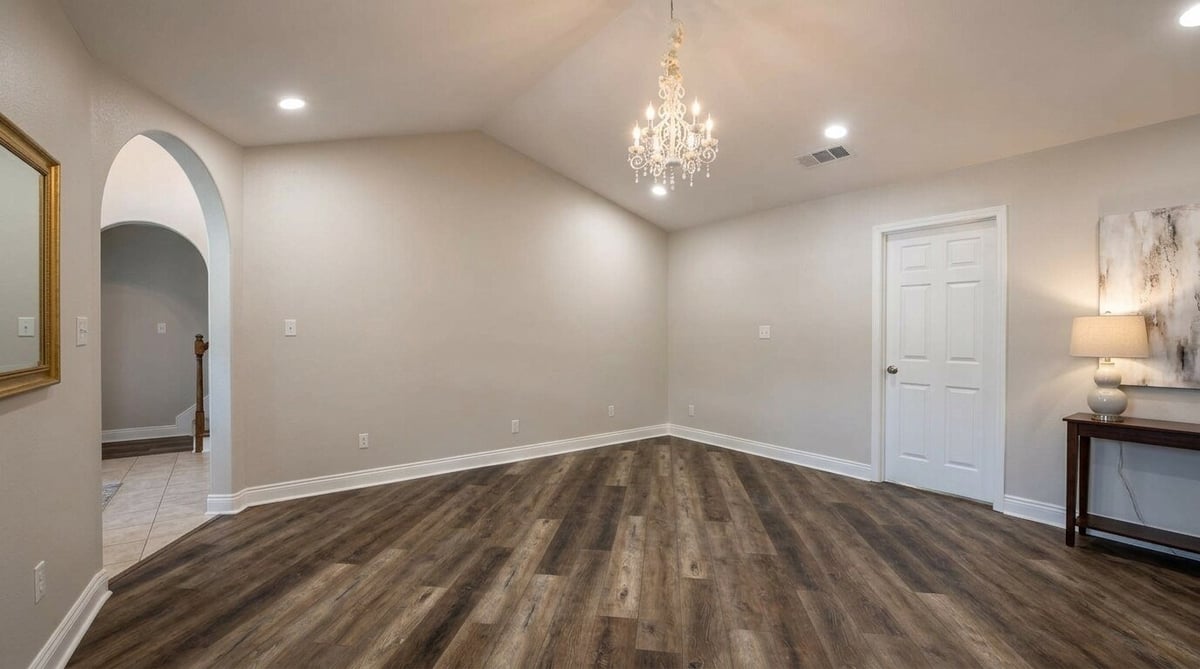 Spacious empty room with dark wood flooring, beige walls, crystal chandelier, arched doorway, and modern white trim