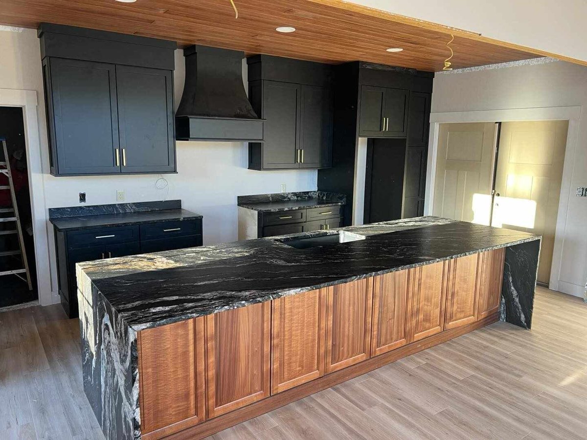 Modern kitchen with dark cabinetry, black marble countertops, large island with wood base, and wood ceiling