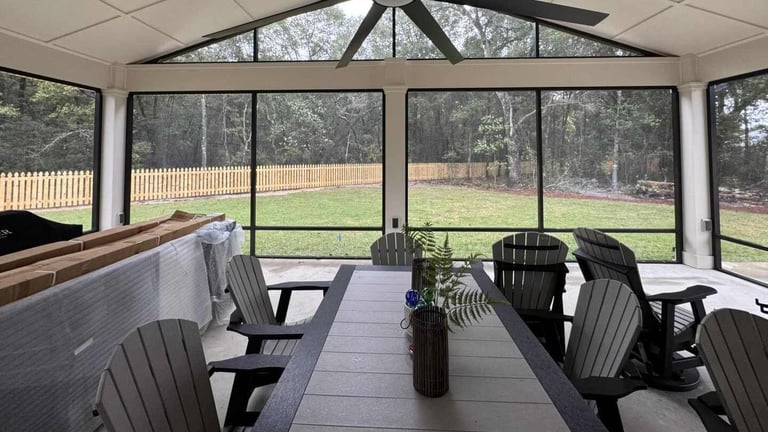 Interior of a screened porch with black Adirondack chairs, a round table, and expansive views of a grassy backyard through large windows.