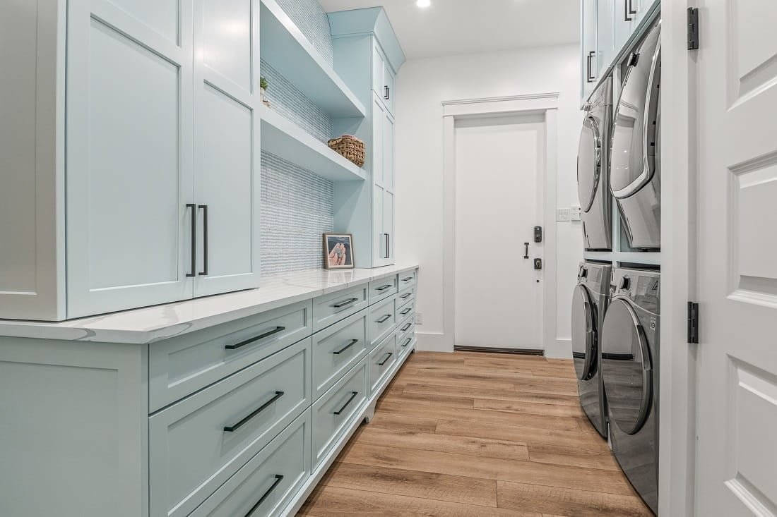 Modern laundry room with light blue cabinetry, stacked washer and dryer, and wooden flooring