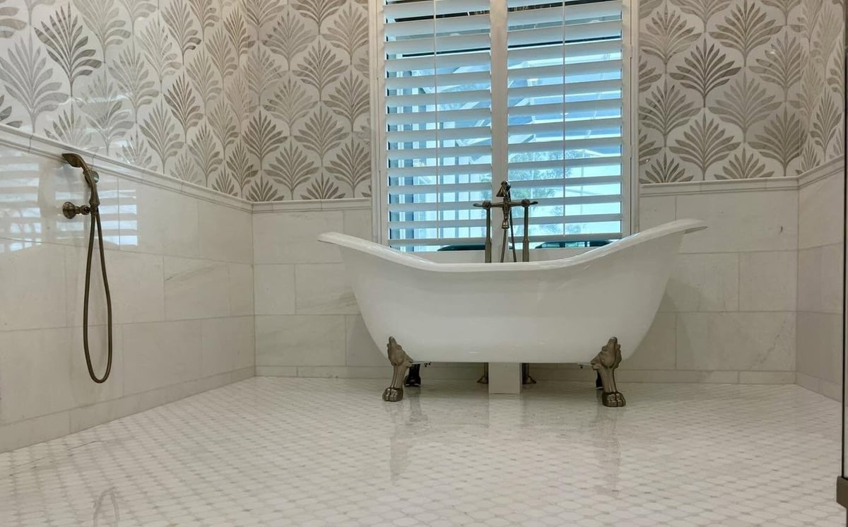 Luxurious bathroom with white clawfoot bathtub, decorative wallpaper, shuttered window, and hexagonal tile flooring