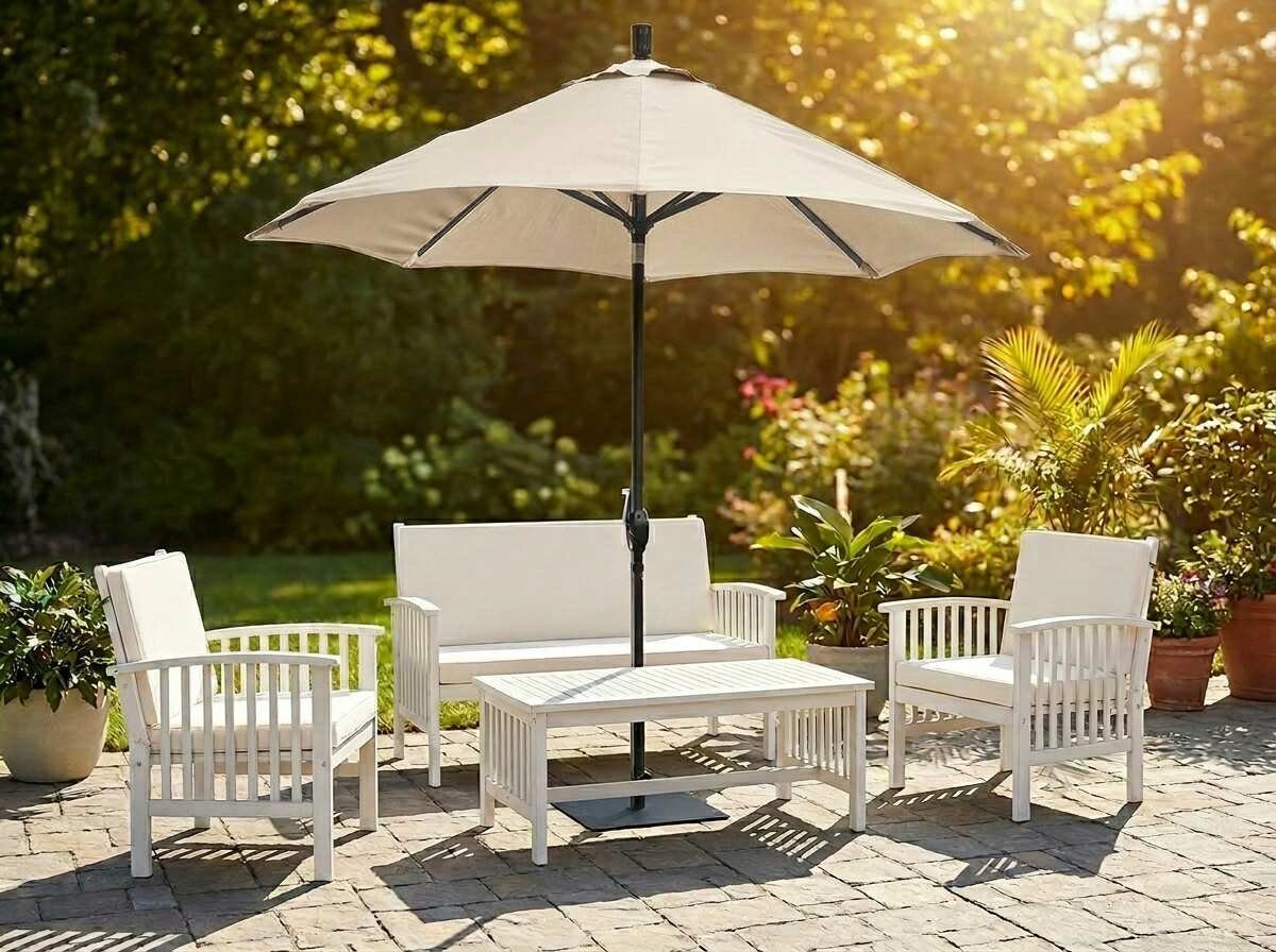 White patio furniture set with umbrella on a stone patio surrounded by green plants and flowers