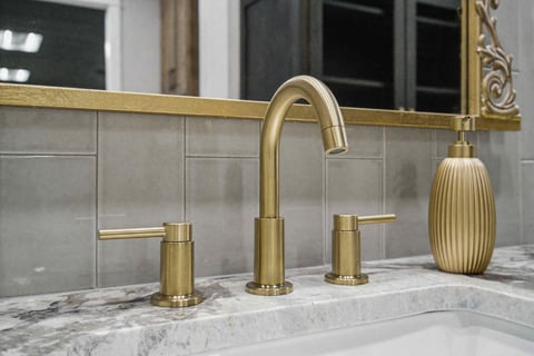 Luxury gold bathroom faucet with marble countertop and tiled backsplash, featuring an ornate framed mirror