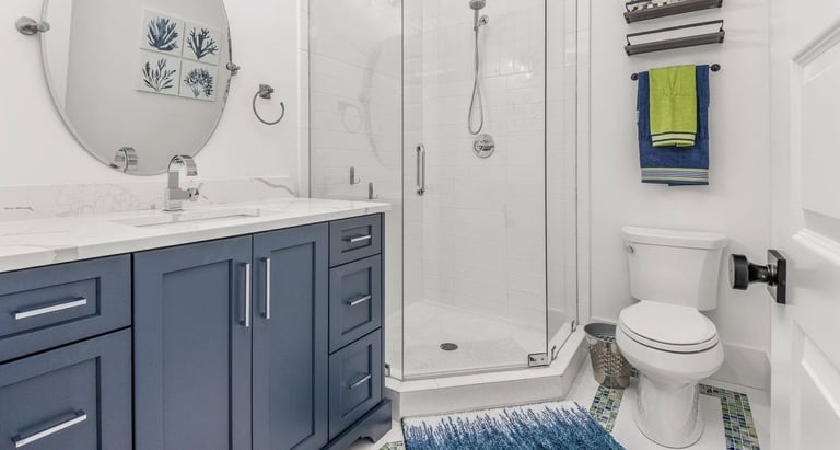 Modern bathroom with blue vanity, white subway tile walls, glass shower enclosure, toilet, and decorative towel rack
