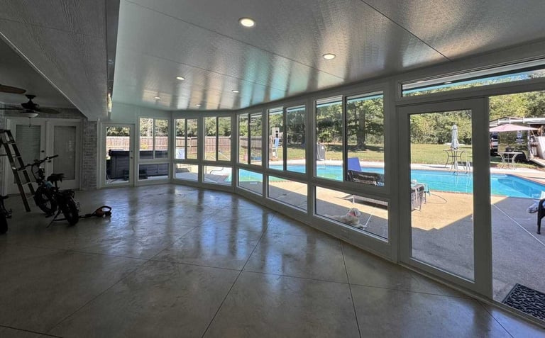 Modern fitness studio with polished concrete floors, large glass doors and windows overlooking an outdoor swimming pool and patio area.