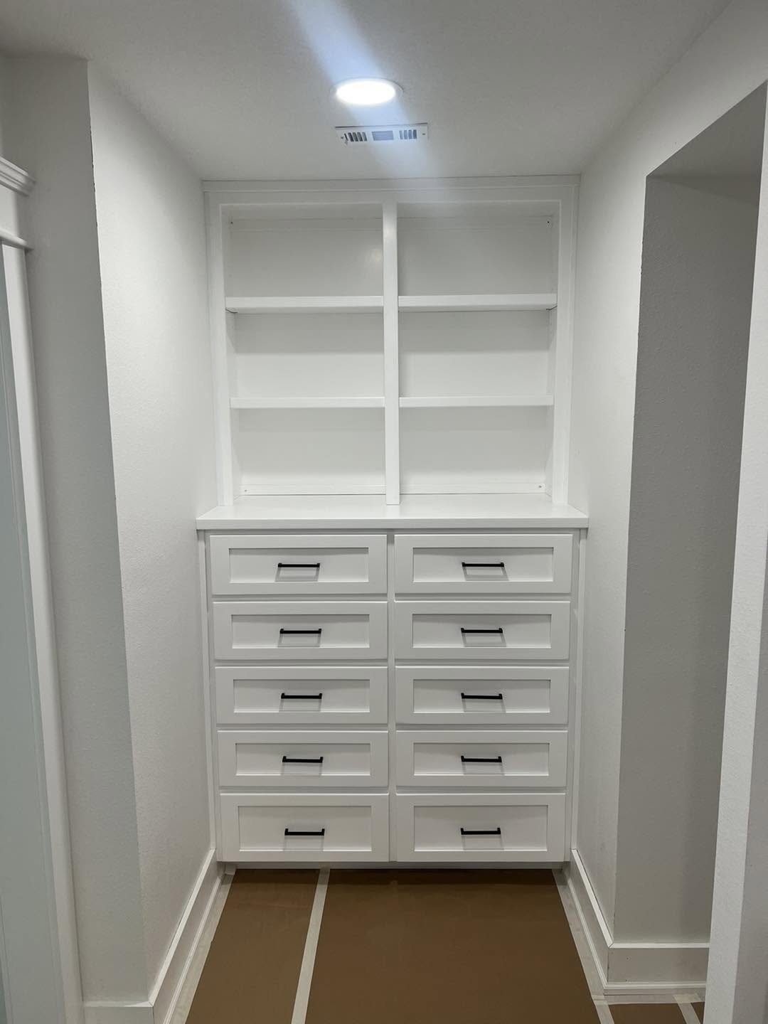 White built-in closet organizer with open shelving on top and ten drawers below in a narrow hallway space.