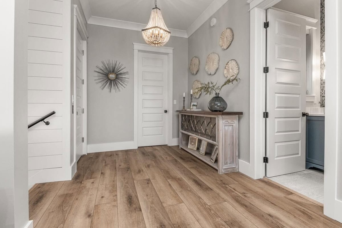 Modern entryway with wood plank flooring, white shiplap walls, white panel doors, chandelier, and white console table with decorative accents
