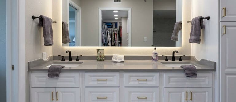 Modern bathroom vanity with dual sinks, white cabinetry, gray countertop, and illuminated mirrors above.