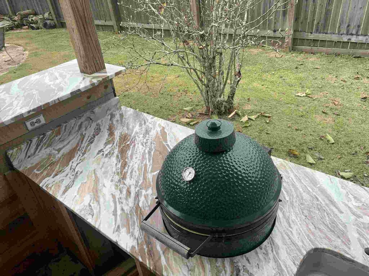 Green ceramic egg-shaped grill in a backyard with metal table and wooden fence