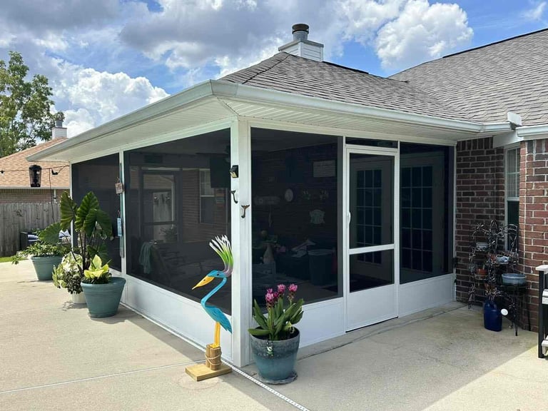 Screened porch addition on brick house with white trim, potted plants, and concrete patio on sunny day