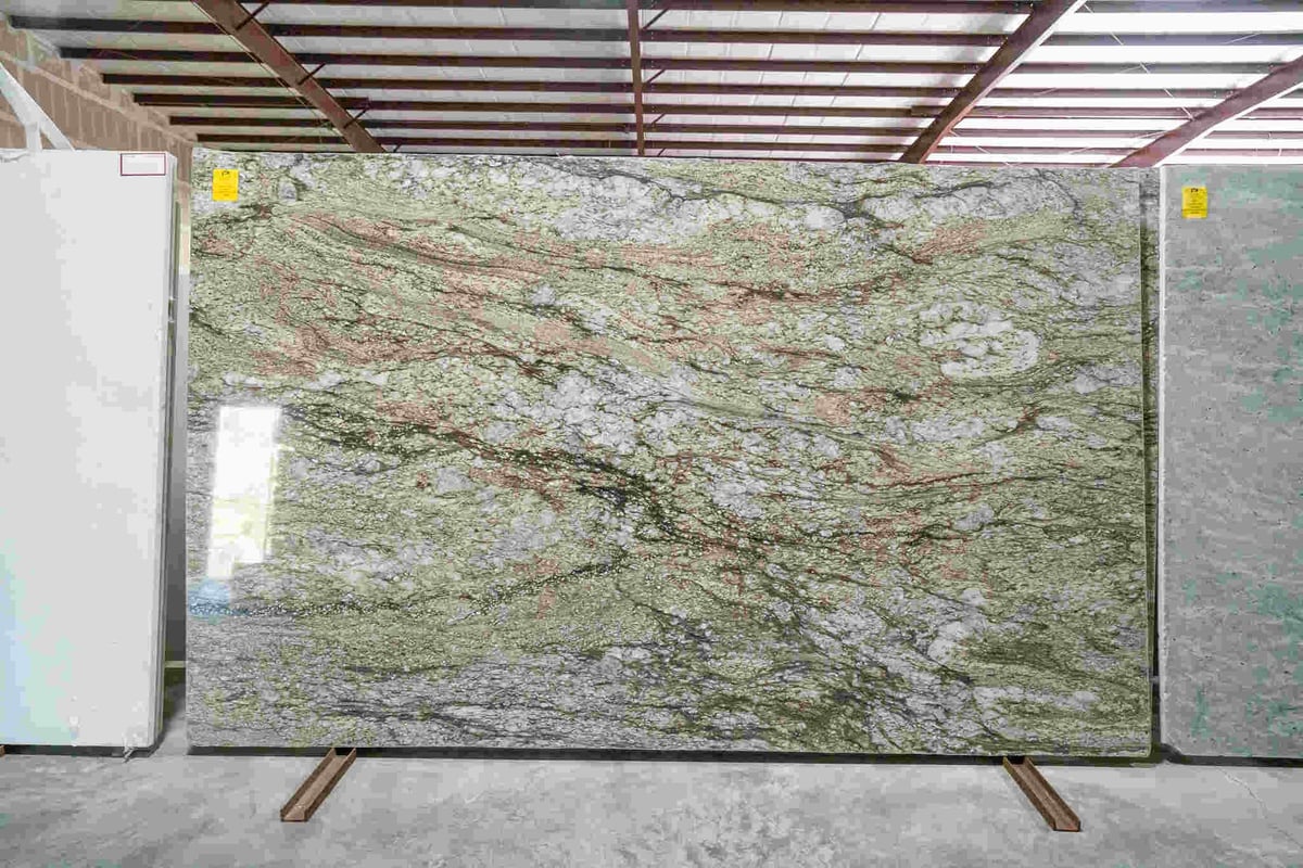 Large green and white marble slab on display in a stone showroom with metal frame overhead and other material samples visible