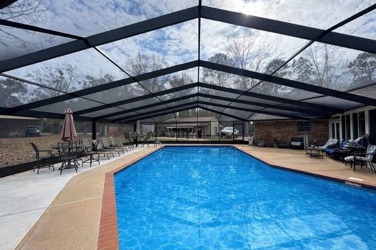 Indoor swimming pool with bright blue water under a black glass-paneled ceiling, surrounded by lounge chairs and a brick building