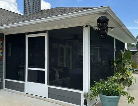 Modern screened porch with white trim and dark screens, potted plants nearby, attached to residential house under clear sky