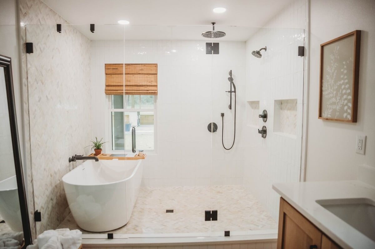 Modern bathroom with white soaking tub, large walk-in shower with marble tile, and wood vanity cabinetry.