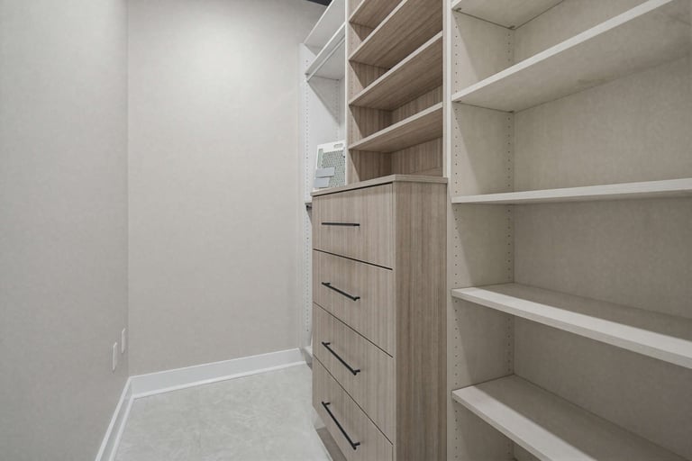 Modern walk-in closet with white shelving units, wooden dresser with drawers, and empty storage compartments