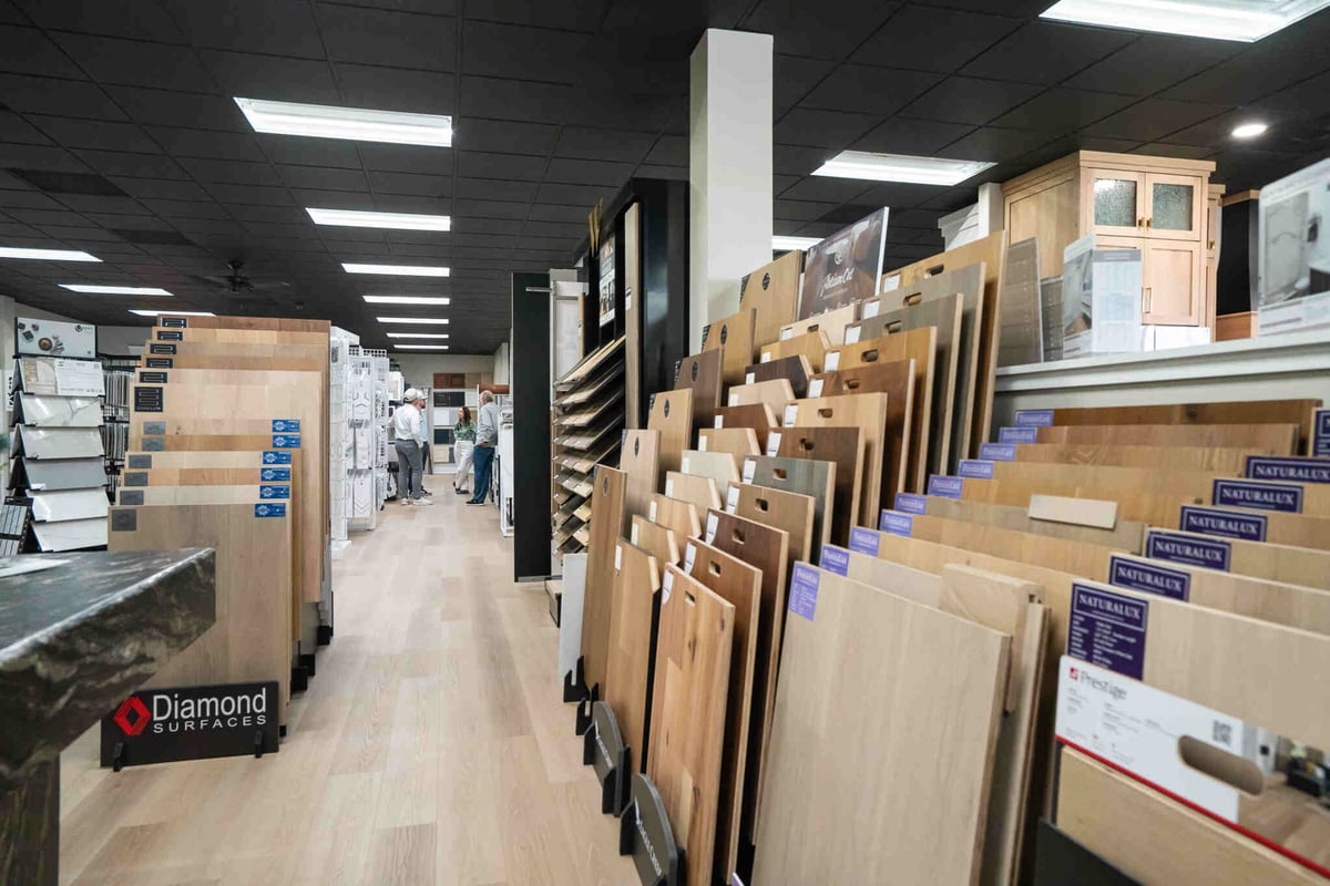 Interior of a flooring showroom displaying various wood and laminate samples organized on racks and display stands under bright ceiling lights